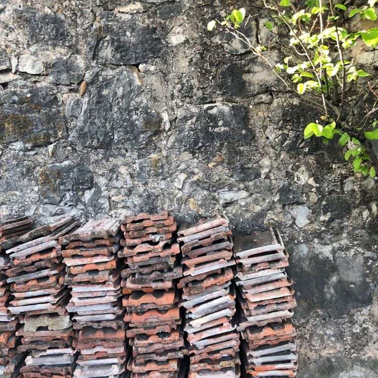 muro de piedra natural sobre el que se apoyan pilas de tejas antiguas